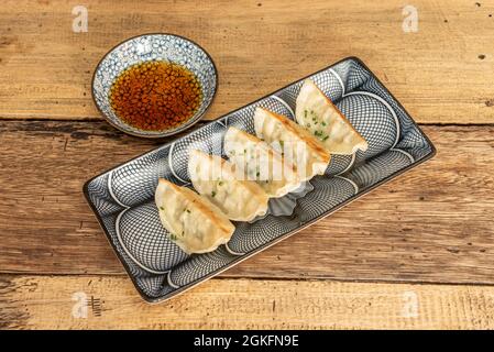 porzione di gyozas fritto sul grill, dim sum, con salsa di soia, erba cipollina tritata su piatti decorati Foto Stock