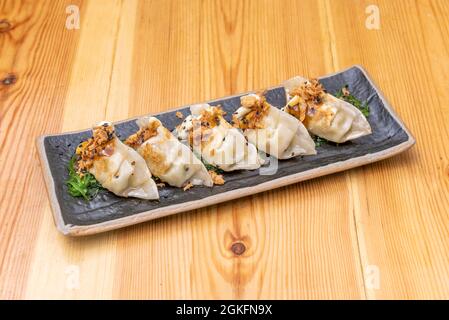 Grandi gnocchi giapponesi, gyozas, fritti alla griglia ripieni di carne e serviti con alghe di wakame su un piatto nero Foto Stock