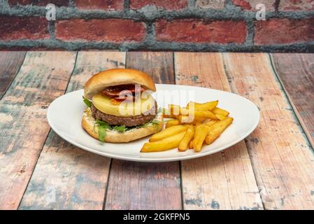 Hamburger italiano con un letto di rucola, formaggio e pomodoro disidratato con una guarnitura di patatine fritte fatte in casa e un piatto bianco Foto Stock