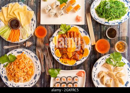 Immagine della vista dall'alto di un piatto di cibo cucinato in un ristorante cinese con tagliatelle di udon, anatra all'arancia, anatra di Pekin, makis di salmone, bacchette, gyozas, wakame Foto Stock