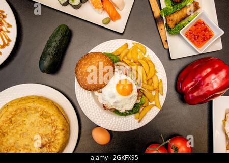 Hamburger con uova fritte, frittata di patate, cetrioli e peperoni su tavola grigia Foto Stock