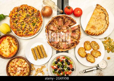 Immagine dall'alto di piatti italiani, calzone ripiene, pizza con pancetta, pane all'aglio, insalata mediterranea, bastoncini di mozzarella, pomodoro e cipolla, oliv Foto Stock