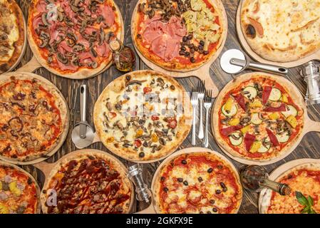 Set di pizza intera su tavola di legno. Barbecue, funghi con prosciutto, verdure con ananas, formaggio e guanciale, forchette e taglierine per pizza Foto Stock