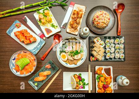 Immagine vista dall'alto di piatti asiatici con sashimi di salmone con avocado, pesce e ramen di verdure, vassoi assortiti di uramaki e maki, California roll, s Foto Stock