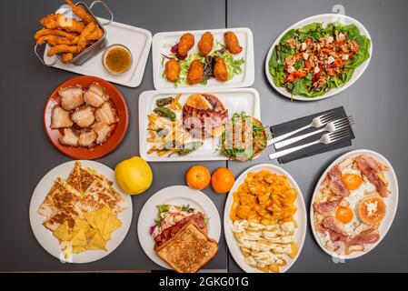 Set di piatti cucinati in un popolare ristorante di tapas spagnole. Crocchette di prosciutto, pancetta fritta, uova spezzate, patata di bravas, hamburger con peperoni, spinaci Foto Stock