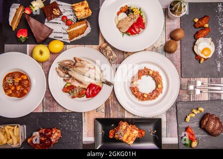 Immagine della vista dall'alto di un delizioso piatto di cibo spagnolo, orata di orata alla griglia, guancia di maiale, ali di pollo con uova fritte, tartare di salmone, insalata di pancia e. Foto Stock