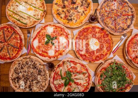 Gruppo di pizze assortite con peperoni, frutti di mare, uova e asparagi verdi, margarita, rucola, pancetta, funghi, acciughe su tavola in legno Foto Stock