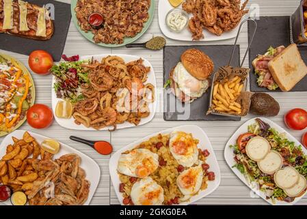 Immagine vista dall'alto di popolari piatti spagnoli e tapas. Ali fritte, calamari, sandwich di calamari, sandwich di pollo, insalata con acciughe. Foto Stock