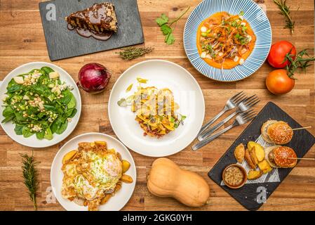 Vista dall'alto di deliziosi piatti mediterranei su un tavolo di legno. Pasta fritta, spinaci e insalata di pinoli, uova fritte con patate. Crema di zucca Foto Stock