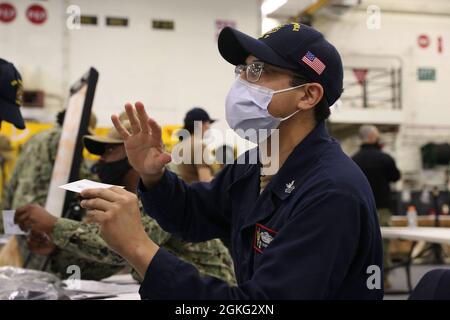 210413-N-CM110-1033 SAN DIEGO (13 aprile 2021) – Ospedale Corpsman 1a classe Daniel Vilchezarrona spiega la scheda di registrazione della vaccinazione COVID-19 nella baia di Hangar a bordo della nave d'assalto anfibio USS Tripoli (LHA 7), aprile 13. I marinai a bordo di Tripoli si sono offerti volontariamente per ricevere le vaccinazioni COVID-19 come parte del proseguimento della prima fase del piano di vaccinazione COVID-19 del Dipartimento della Difesa degli Stati Uniti. Tripoli è casa a San Diego. Foto Stock