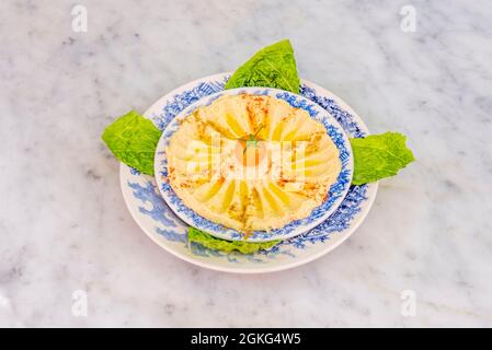 Hummus di ceci con olio d'oliva, paprika, ras el hanout e pomodoro ciliegia e lattuga da bagnare su piatti con bordi blu Foto Stock