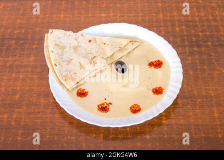 Piatto di hummus con pezzetti di pane azzimo, olive nere e sentori di paprika su tavola di legno Foto Stock