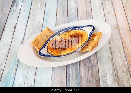 Piatto di porcellana con hummus di ceci, semi di girasole e pomodoro disidratato e paprika in cima accompagnato da alcuni pezzi di pane da immergere Foto Stock