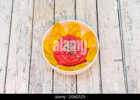 Ciotola bianca di hummus di barbabietola con semi di papavero e semi di sesamo con patatine di banana per l'immersione Foto Stock