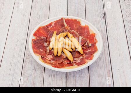 Piatto bianco con sottili fette di prosciutto iberico alimentato con ghiande con punte di campagna sul tavolo luminoso Foto Stock