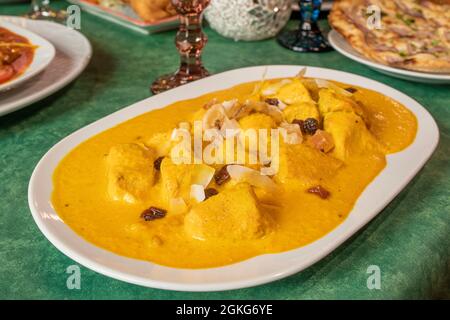 Curry di pollo giallo delicato, korma, cucinato in un ristorante europeo pakistano con frutta secca e uvetta su uno dei tavoli del ristorante. Foto Stock