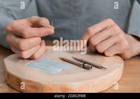 Trattamento di agopuntura sulle mani dell'uomo. Riabilitazione usando medicina alternativa. Strumenti di pressione su sfondo in legno. Foto Stock