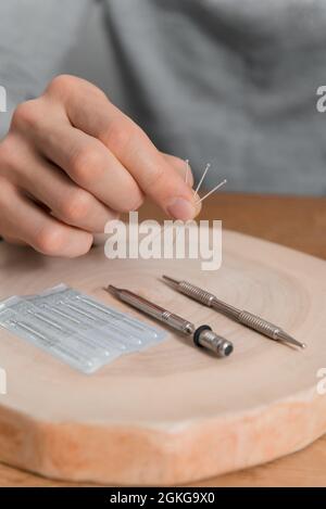 Trattamento di agopuntura sulle mani dell'uomo. Riabilitazione usando medicina alternativa. Strumenti di pressione su sfondo in legno. Foto Stock