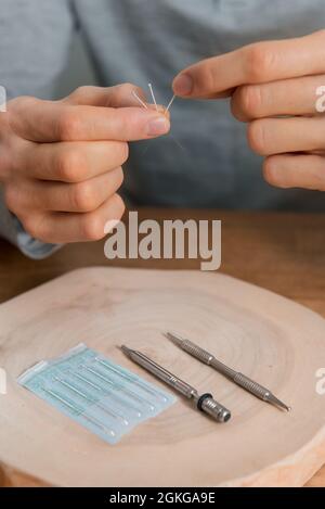 Trattamento di agopuntura sulle mani dell'uomo. Riabilitazione usando medicina alternativa. Strumenti di pressione su sfondo in legno. Foto Stock