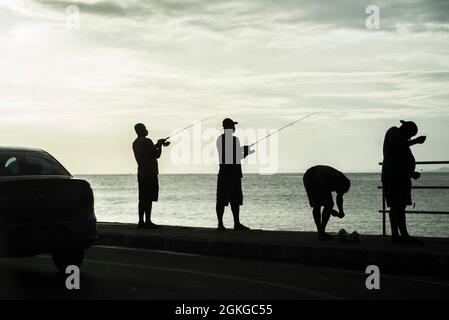 Salvador, Bahia, Brasile - 11 aprile 2021: Silhouette di pescatori con i loro pali al tramonto. Foto Stock