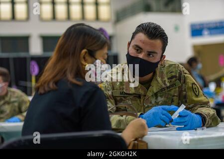 MANGILAO, Guam (16 aprile 2021) – PFC. Enricke Munoz, uno specialista di medaglie di combattimento assegnato alla 25a Divisione di fanteria, spiega la scheda di vaccinazione prima di somministrare un vaccino COVID-19 a supporto del team di vaccinazione COVID-19 del Dipartimento di Sanità pubblica e servizi sociali Guam (DPHSS) presso una clinica di vaccinazione tenuta presso la Field House dell'Università di Guam Calvo. Il comando IndoPacifico degli Stati Uniti, attraverso l'Esercito Pacifico degli Stati Uniti, continua a fornire supporto flessibile al Dipartimento della Difesa dell'Agenzia federale per la gestione delle emergenze come parte della risposta dell'intero governo al COVID-19. Foto Stock