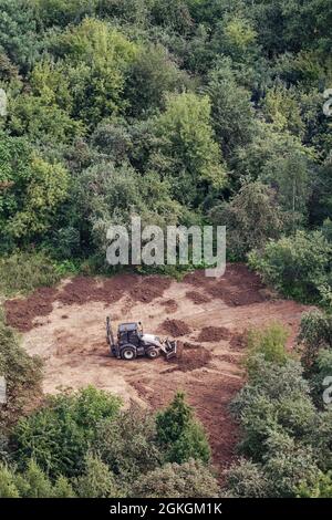 L'escavatore prepara il terreno sul campo nella foresta tra gli alberi per il paesaggio e l'agricoltura, vista dall'alto Foto Stock