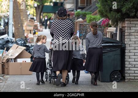 Una madre hasidica e 3 figlie, tutte vestite modestamente e in modo molto simile in bianco e nero. Su una strada a Williamsburg, Brooklyn, New York City Foto Stock