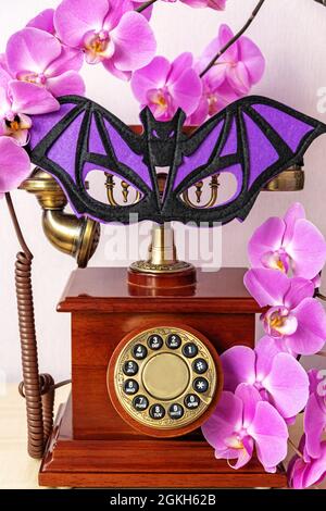 Maschera a forma di pipistrello sul telefono vecchio stile con fiori di orchidea Foto Stock