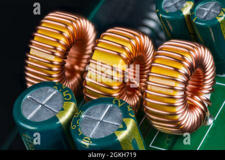 Nuclei di ferrite gialli di induttori toroidali avvolti con filo di rame su scheda a circuito stampato verde. Primo piano di bobine o condensatori elettrolitici su circuito stampato. Foto Stock