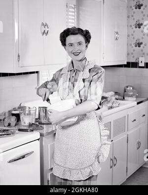 1950S SORRIDENTE BRUNETTE DONNA CASALINGA INDOSSARE GREMBIULE IN CUCINA MESCOLANDO UNA CIOTOLA DI PASTELLA GUARDANDO LA MACCHINA FOTOGRAFICA - H962 HAR001 HARS HOME VITA COPIA SPAZIO MEZZA LUNGHEZZA SIGNORE PERSONE CURA FIDUCIA MIX B&W PASTELLA OCCHIO CONTATTO BRUNETTE SUCCESSO OMEMAKER SOGNI AGITARE FELICITÀ HOMEMAKERS ALLEGRO TEMPO LIBERO FORZA AGITAZIONE SCELTA DI SCELTA DI PROGRESSO RICREAZIONE ORGOGLIO AUTORITÀ CASALINGHE OCCUPAZIONI SORRISI CONCETTUALE GIOIOSO ELEGANTE CREATIVITÀ MEDIO-ADULTO DONNA DI MEDIO-ADULTO DI PRECISIONE BIANCO E NERO ETNIA CAUCASICA PREPARAZIONE ALIMENTARE HAR001 VECCHIO STILE Foto Stock