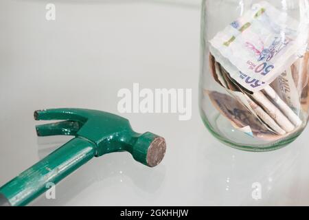 martello vicino al vaso di vetro pieno di banconote. martello per rompere il porcellino di vetro banca. concetto di economia e risparmio personale Foto Stock