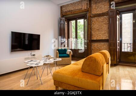 Soggiorno con decorazioni contemporanee in un edificio d'epoca. Area TV con muro di mattoni a vista in un appartamento in affitto per le vacanze Foto Stock