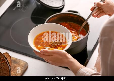 Donna che versa il borscht delizioso dalla pentola di cottura alla ciotola in cucina Foto Stock