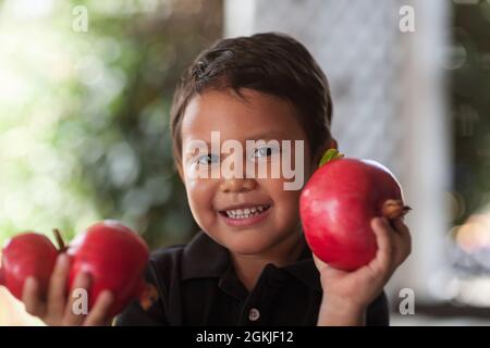 Sorridendo il bambino che tiene in su nelle sue mani piccole alcuni melograni freschi tagliati che sono coltivati organicamente. Foto Stock