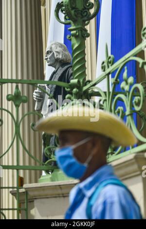 San Salvador, El Salvador. 14 settembre 2021. Un uomo indigeno si erge accanto a una statua raffigurante Cristoforo Colombo al Palazzo Nazionale, durante la dimostrazione. I membri della comunità indigena Nahuizalco protestano contro la Giornata dell'Indipendenza Bicentenaria di El Salvador, definendola indipendenza per i ricchi. Il 15 settembre l'America Centrale commemora il 200° anniversario dell'Indipendenza dalla Spagna. (Foto di Camilo Freedman/SOPA Images/Sipa USA) Credit: Sipa USA/Alamy Live News Foto Stock