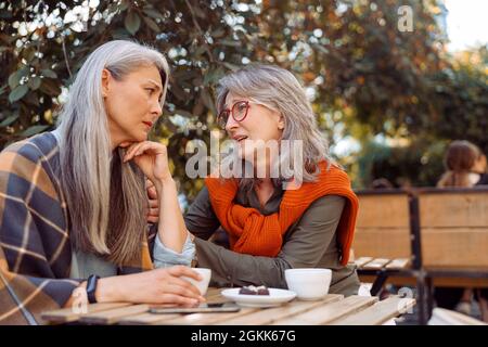 La donna anziana di Comparionate allietera un amico asiatico turbato seduto insieme in Street cafe Foto Stock