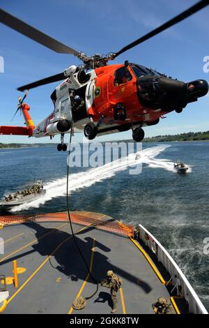 Gli equipaggi della Guardia Costiera con il team di risposta alla sicurezza marittima West utilizzano più risorse, lavorando con un equipaggio di elicotteri Columbia River MH-60 Jayhawk del settore, per salire a bordo di Pierce County Ferry Steilacoom II durante un esercizio tattico il 13 maggio vicino a Fox Island, WA. Questo esercizio è stato svolto per mostrare le competenze e l'interoperabilità multiunità di MSRT West in caso di minaccia di emergenza. Foto Stock