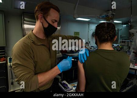 PACIFIC OCEAN (14 maggio 2021) Hospital Corpsman III Classe Andrew Goedde, di Evansville, Ind., somministra un vaccino a bordo della nave d'assalto anfibio USS Essex (LHD 2), maggio 14. Marinai e marines dell'Essex Amphibious Ready Group (ARG) e dell'XI Marine Expeditionary Unit (MEU) sono in corso al largo delle coste della California meridionale. Foto Stock