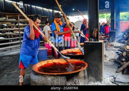 I lavoratori della fabbrica tradizionale di torte, vale a dire Keranjang e Dodol torte, stanno impastando l'impasto che viene cucinato su una stufa a legna. Foto Stock