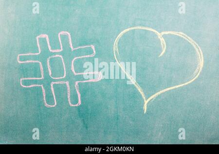 L'amore hashtag è disegnato in gesso rosa sul bordo della scuola. Cartello hashtag e cuore disegnato sulla lavagna della scuola Foto Stock