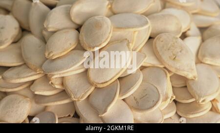 I dadi con la buccia semi di zucca sono ruotare su di una tavola in una piastra. Snack nel piatto trasparente isolato su un sfondo bianco sono la filatura in movimento. Foto Stock