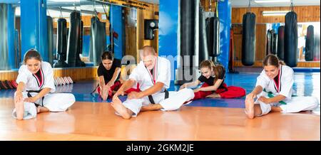 Persone sportive in kimonos che si allungano prima di arti marziali di allenamento in palestra Foto Stock