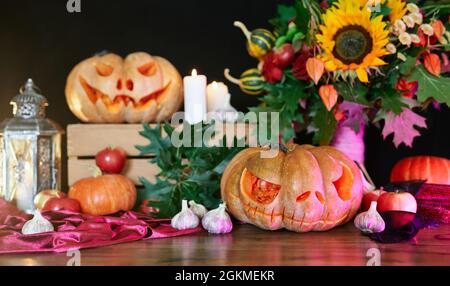 Zucche d'arancia di Halloween con faccia spaventosa. Autunno Fall concetto: Zucche, candele, girasole, foglie, lanterna e altri attributi al tavolo come sfondo tema Halloween. Foto di alta qualità Foto Stock