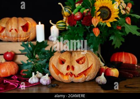 Concetto di Halloween: Zucche, candele, girasole, foglie, lanterna e altri attributi al tavolo come sfondo tema Halloween. Zucca di Halloween con faccia spaventosa. Foto di alta qualità Foto Stock