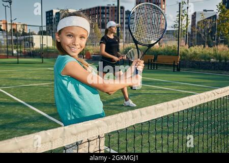 Ritratto di bambino sorridente mentre gioca e pratica il tennis sul campo da tennis con la sua madre allenatore insieme Foto Stock