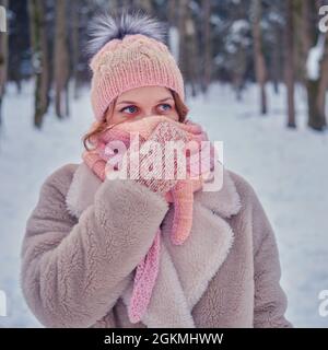 Una donna sorridente si avvolge in abiti che si riscaldano in una foresta invernale con alberi nella neve Foto Stock