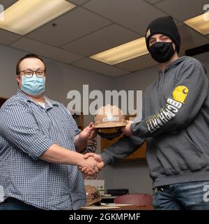 PORT ORCHARD, Washington (28 maggio 2021) – Ryan Reinke, General Foreman, Marine Machinist Shop, Trident Refem Facility Bangor (TRFB), presenta Jeremiah Milliron, Senior, South Kitsap High School (SKHS), con un elmetto a SKHS maggio 28. Il personale di leadership di TRFB ha lavorato con i consulenti di SKHS per identificare tre anziani altamente motivati della scuola superiore che hanno un interesse nel lavoro commerciale e li ha intervistati per un potenziale impiego a TRFB. Foto Stock