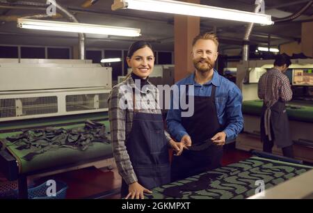 Due simpaticanti calzolai sorridenti che guardano la macchina fotografica in piedi alla scrivania dell'officina Foto Stock