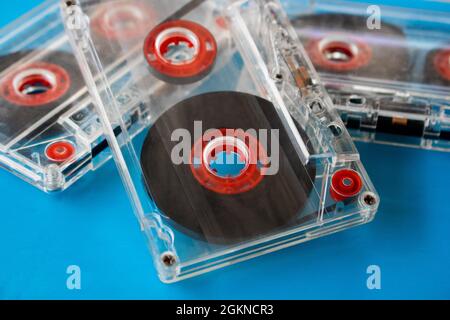 Diverse cassette audio compatte trasparenti con nastro visibile e bobine interne rosse poste casualmente su sfondo blu. Tecnica di messa a fuoco selettiva Foto Stock