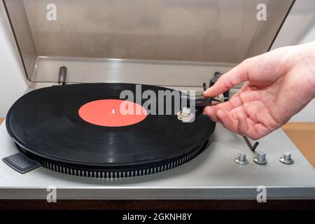 Accensione manuale su giradischi stereo analogico retro vintage. Un giradischi in plastica vecchio stile che riproduce una traccia musicale, vista frontale. Concetto di musica retrò Foto Stock